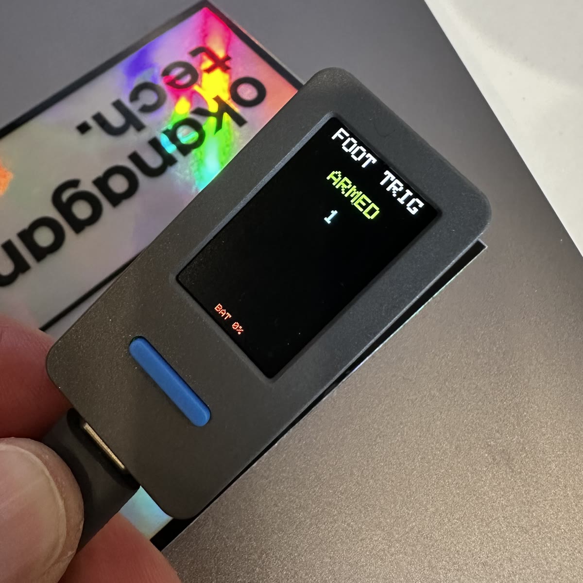 The same device, its screen now reading FOOT TRIG, ARMED in green, with the tap counter at 1.